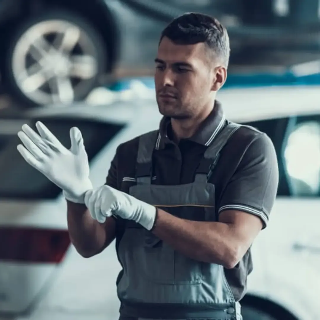 Young male mechanic putting on gloves before an mot test at a centre in Leeds, Yorkshire. 